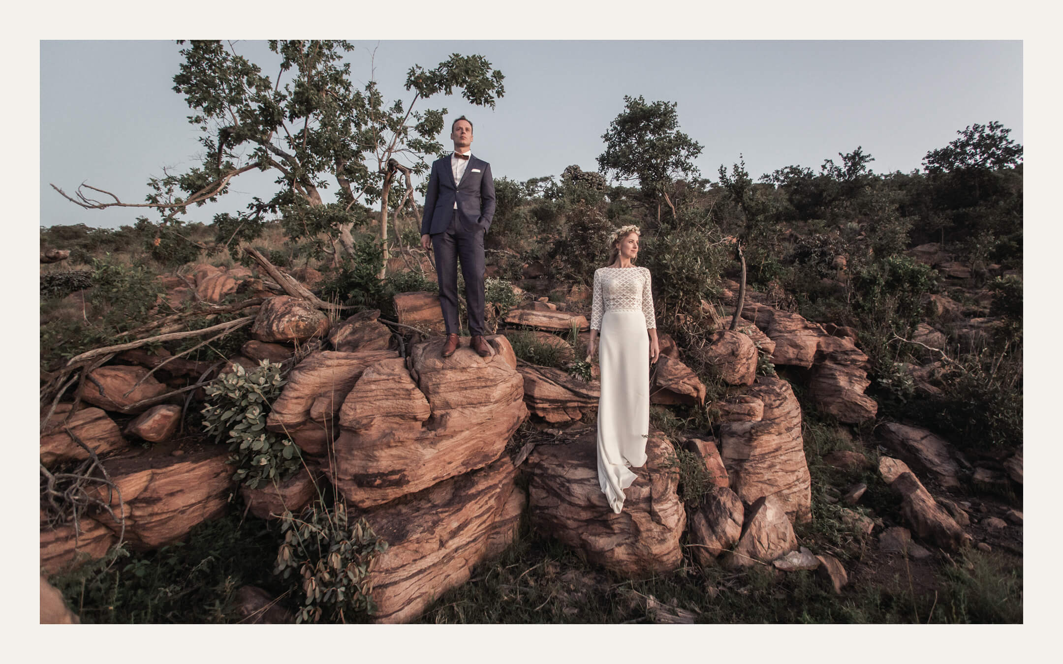 Couple standing apart on red rock outcrops in the bush at last light. Ben Viljoen Photography