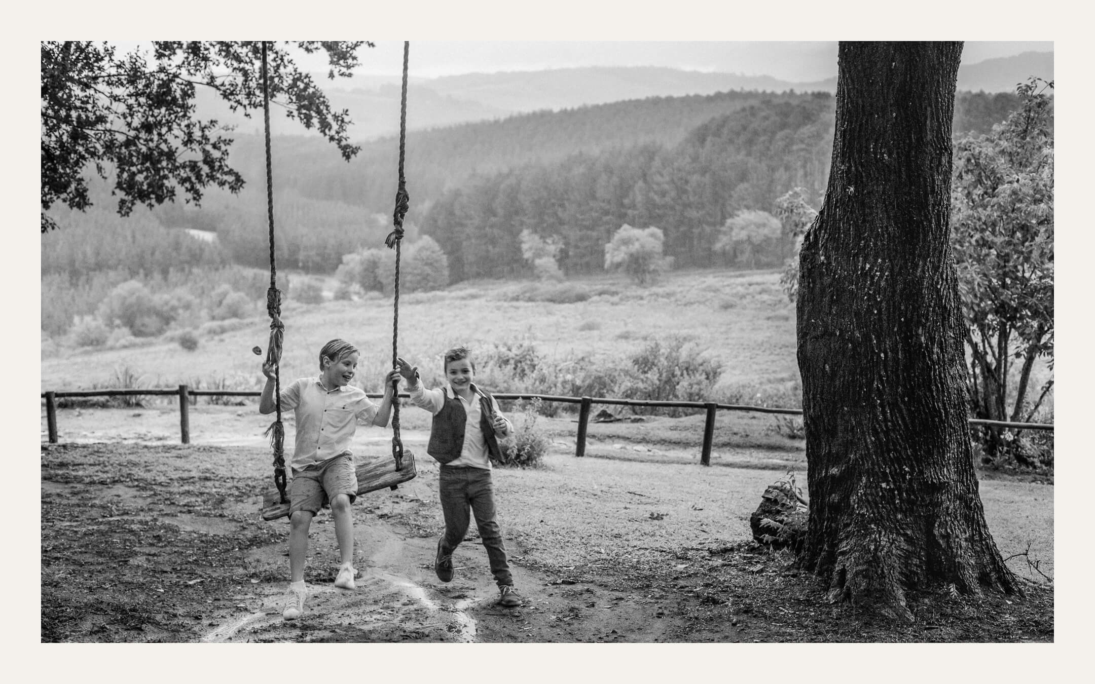 Two boys on a rope swing under a tree above a misty valley. Ben Viljoen Photography