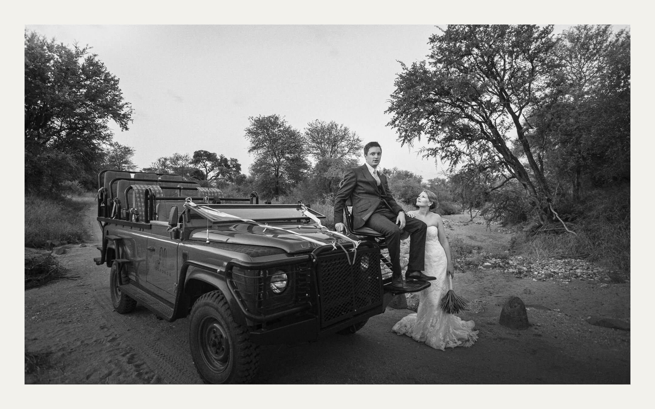 Bride and groom resting on a safari vehicle in a dry riverbed. Ben Viljoen Photography